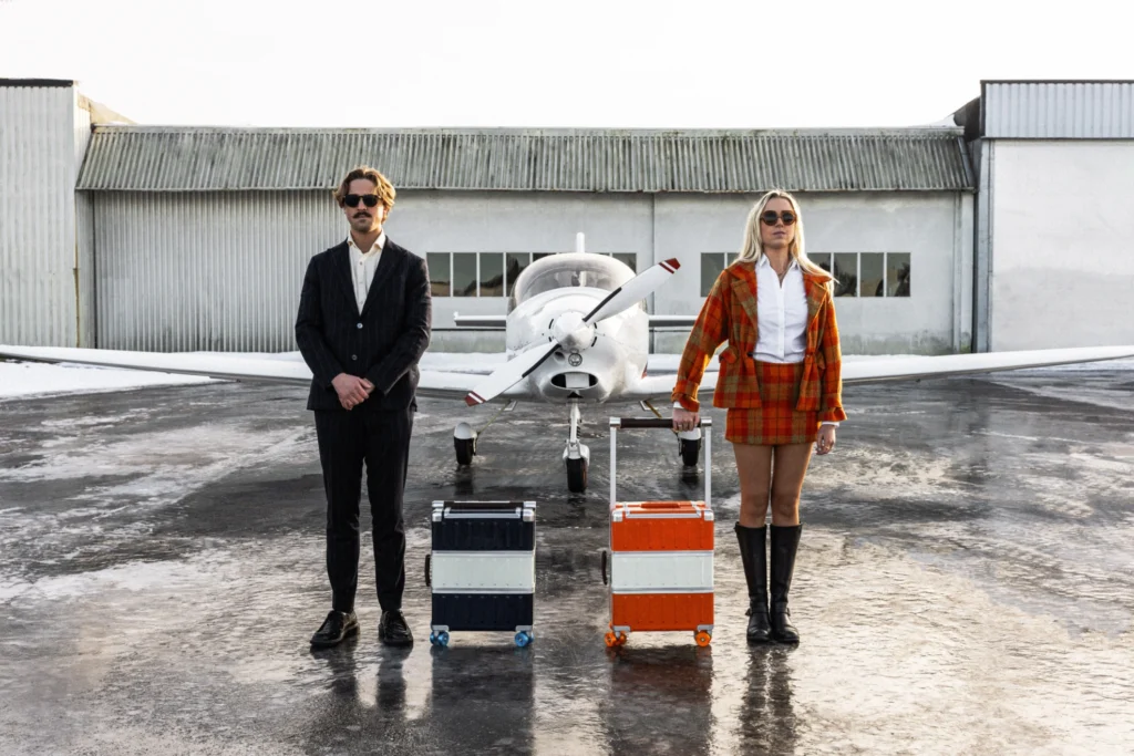 Milla Lack and her brother stand in front of a small propeller plane, each beside a Drobe Cabin, one blue and one orange.